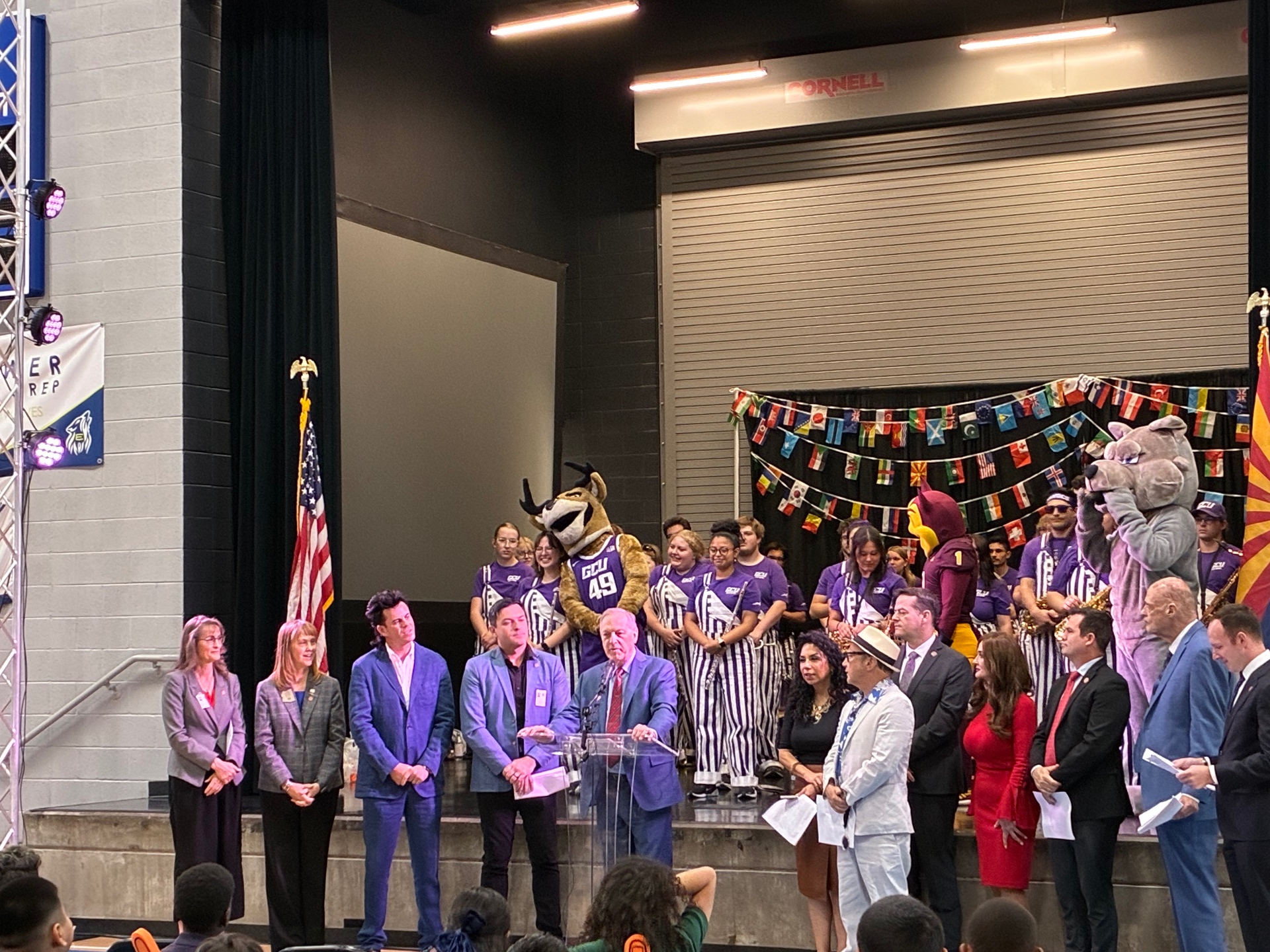 Arizona officials and GCU band on stage at a school event with mascots and international flags